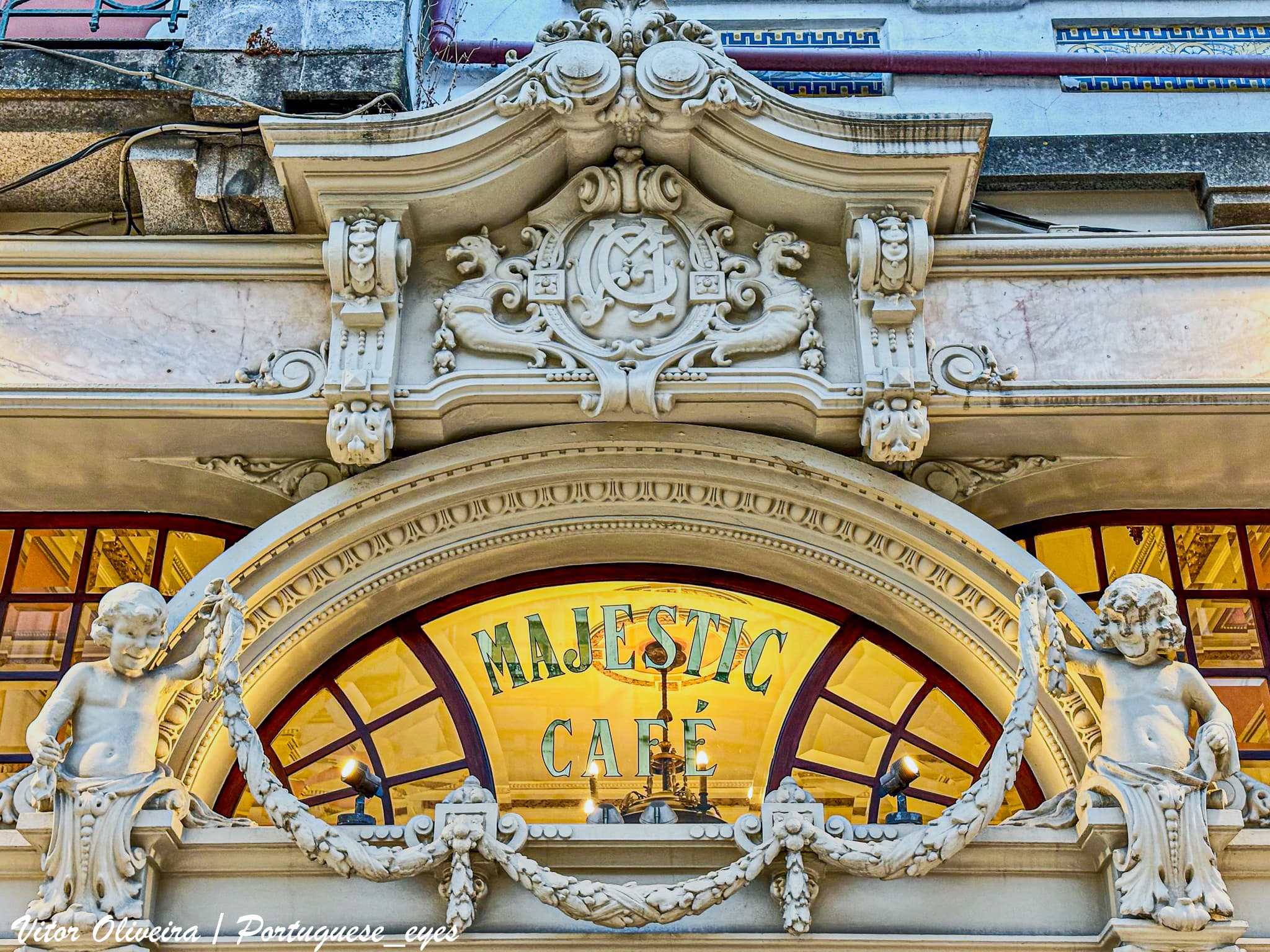 As origens do Majestic remontam, efetivamente, a 17 de dezembro de 1921, quando foi constituída, por um grupo de comerciantes do Porto, a Sociedade por Quotas Café Elite Limitada, que, nesse mesmo dia, assinou um contrato de aluguel do rés-do-chão do prédio situado na Rua de Santa Catarina, números 110 a 116, "destinado à montagem de um café, cervejaria". Este contrato teria início em 1 de junho de 1922. No entanto, foi apenas quase um ano depois, em 2 de dezembro de 1922, que ocorreu a inauguração ao público do “feérico e deslumbrante conjunto do Majestic Café”, cuja autoria ficou a cargo do arquiteto senhor José Pinto de Oliveira. (Fonte: Commércio do Porto, “Os grandes estabelecimentos do Porto. Inauguração do Majestic-Café”, 2 de dezembro de 1922.) Desde a sua abertura, o café manteve o nome de Majestic Café. Em 4 de dezembro de 1924, a Sociedade Café Elite Lda, sua proprietária, foi substituída pela sociedade Majestic Café Lda. Em 30 de julho de 1925, um pedido para a "construção de um bar (...) com frente para a Rua de Passos Manuel, onde será vendido Vinho do Porto" foi apresentado à Câmara Municipal do Porto. O estilo regional da nossa arquitetura foi escolhido para a construção do bar, projeto assinado pelo arquiteto João Queiroz. (Fonte: Requerimento para licenciamento de obras, apresentado pela empresa Majestic Café Lda e assinado pelo arquiteto João Queiroz, em 30 de julho de 1925. Carimbo de licença nº 1319 de 27 de setembro de 1925. Arquivo de Obras da Câmara Municipal do Porto.) Mais do que um café, o Majestic conta a história do Porto: o Porto dos anos vinte, das tertúlias políticas e do debate de ideias; o Porto da "Belle Époque", dos escritores e artistas. Situado na Rua de Santa Catarina, a avenida pedonal de comércio e passeio da sociedade de então e de agora, iluminava o passeio com sua decoração Arte Nova. Lá dentro, inalava-se o perfume dos bancos aveludados e das madeiras envernizadas, enquanto os cinco sentidos se confundiam nos tetos de gesso decorado e na abundante espelharia em cristal flamengo. Mármore e metal se uniam com requinte inigualável. Nos fundos, a natureza espreitava através do jardim de Inverno, que ligava a Rua de Santa Catarina à Rua de Passos Manuel. Nesse dia, já distante, a inauguração ficou marcada na cidade. Muitos se dirigiram a esse ponto da cidade para conhecer o novo edifício que se incrustava na paisagem arquitetônica portuense. O café agradou a intelectuais e boêmios, mas também às senhoras da melhor sociedade que, em passeio, ali tomavam o chá ou um sorvete. O café recebeu honras e distinções, incluindo uma visita distinta do piloto aviador, e mais tarde almirante, Gago Coutinho, que estava sempre acompanhado de belíssimas mulheres e acabara de retornar de mais uma arriscada jornada à ilha da Madeira. Ele ficou tão agradavelmente surpreendido com o esplendor do novo estabelecimento que retornou várias vezes para contemplar a beleza de todos os detalhes, uma das quais na companhia da famosa atriz Beatriz Costa. O glamour e a elite cultural parisiense eram referências para a cultura portuguesa da época e influenciaram a escolha do nome – Majestic – impregnado de charme da "Belle Époque". Neste espaço, passaram a convergir figuras intelectuais da cidade. José Régio, Teixeira de Pascoaes, Leonardo Coimbra, entre outros, emprestaram à casa a literacia necessária para que se desenrolasse aceso debate entre figuras públicas e aquelas que viriam a ser, sobre as questões políticas, sociais e filosóficas mais prementes. Num lugar que é, por mérito próprio, arte, não poderiam faltar aqueles que a constroem. Alunos e professores da Escola de Belas Artes do Porto juntavam-se a artistas renomados, como Júlio Resende, para desbravar novos caminhos e motivações artísticas, propor rupturas, criticar formalismos, conceitualizar novas formas ou simplesmente ouvir o que se dizia na época. Em vários cafés do Porto ocorria o mesmo que no Majestic: uma intensa polarização social da cultura, ao sabor do café ou do absinto escondido. Nos anos 60 do século XX, coincidindo com um certo adormecimento forçado das manifestações culturais do país, o Café Majestic começou a adormecer. Este declínio foi lento, mas contínuo. O estado de degradação a que estava sujeito logo começou a ser percebido pelas forças vivas da cidade. Assim, em 31 de agosto de 1981, foi decretado Imóvel de Interesse Público. Dois anos depois, a nova gerência estudou formas de devolver o café à cidade. Entretanto, o tempo mostrou sua inexorabilidade, e os anos de incúria transformaram o espaço em um local sombrio. O Majestic e toda a história que suas xícaras tiveram que beber clamavam por reconhecimento. Em 1992, 70 anos após a inauguração, decidiu-se devolver-lhe a vaidade justa de ser um dos mais belos cafés do Porto. A 15 de julho de 1994, reabriu suas portas, sendo necessários dois anos para restaurá-lo. Quem entra agora encontra exposições, eventos e até mesmo um certo mediatismo, pois às vezes é palco de gravações televisivas. O Café Majestic, de traça ideada pelo arquiteto José Pinto de Oliveira, permanece até hoje como um dos mais belos e representativos exemplares de Arte Nova na cidade do Porto. O edifício, fundado em 1916 no ângulo formado pelas ruas de Santa Catarina e Passos Manuel, previa, na memória descritiva de sua reconstrução, a existência de estabelecimentos voltados para a rua pedonal. A imponente fachada em mármore, adornada com aspectos vegetalistas de formas sinuosas, reflete o bom estilo decorativista da época. Um trio de elegantes portadas marca a frontaria, limitada por uma seção retangular, em vidro. No topo, um frontão coroa a composição com as iniciais do Majestic. Ladeiam-no duas representações de crianças que, divertidas, convidam o transeunte a entrar. Dentro do estabelecimento, de planta retangular, reina a linguagem Arte Nova. A simetria curvilínea das molduras em madeira e os detalhes decorativos cativam a observação. Grandes espelhos riscoçados pela idade, intercalados por candeeiros em metal trabalhado, delimitam as paredes em um inteligente jogo óptico de amplitude, que lhe dá uma dimensão maior do que a real. Esculturas em estuque, representando rostos humanos, figuras desnudas e florões, confirmam o gosto ondulante e sensual, enquanto duas linhas de bancos em couro gravado, substituindo os originais em veludo vermelho, criam, em termos de perspectiva, uma sensação de profundidade e elegante aconchego. O contorno sinuoso dos caixilhos da espelharia, a luminosidade dos candeeiros, os detalhes em mármore e os bustos sorridentes que se estendem das paredes ao teto conferem-lhe uma ambiência dourada e confortável, incitando ao repouso e à conversa amena. O Café Majestic emana uma atmosfera de luxo, requinte e bem-estar. O pátio interior, construído em 1925, é um recanto de contornos delicados, com escada e balaustrada de pequenas dimensões, arquitetado como um jardim de Inverno. Sob a direção do mestre Pedro Mendes da Silva, este espaço simboliza uma nova era do Café Majestic. A construção do bar e da ligação ao café por meio de uma escadaria permitiu abrir uma nova frente, a da Rua Passos Manuel, "onde será vendido vinho do Porto. Para isso, escolheu-se o estilo regional da nossa arquitetura, não só para a construção do bar, mas também para a vedação do muro". A nova fachada foi subsequentemente idealizada e executada seguindo moldes diferentes dos adotados para o interior. Se este é de gosto internacional, o novo espaço, sem o renegá-lo, apresenta um estilo mais rústico, manifestando o que mais tarde Raul Lino designou como casa portuguesa. Nesse mesmo ano, o Majestic singularmente cumpriu a função plural de satisfazer todos os desejos da clientela. Voltou a chamar o arquiteto João Queiroz, desta vez para abrir uma modesta, mas graciosa janela no muro remodelado, voltada para a Rua Passos Manuel, onde passará a vender tabaco e rapé à população. Um ano depois, em 1926, o espaço foi ampliado e cedido à exploração da firma Tinoco & Irmãos, construindo uma "pequena cabina (…) para servir de tabacaria". Auspícios de novos tempos e hábitos surgiram em 1927, através da ampliação do bar com vista ao "serviço e fornecimento de cerveja para o terraço já existente". O espaço, como o vemos, apresenta-se evolutivo. Desde uma formulação mais depurada e arquitetônica na entrada, movida pelas raízes Beaux Arts do arquiteto, até chegarmos ao jardim, passamos por um decorativismo que colmata as estruturas arquitetônicas, terminando no portal jônico de ligação ao exterior, com grandes volutas transparentes e sensuais, tipicamente Art Nouveau, insinuando as esculturas femininas que vislumbramos do lado de fora. Esse espaço verdejante e luminoso serve atualmente para a dinamização de concertos durante o verão, tornando-se assim o terceiro centro cultural do Majestic, rivalizando com o piano de cauda no interior e com as inúmeras exposições de pintura acontecendo no piso inferior, outrora dedicado ao jogo de bilhar. Foi também neste ano de 1927 que, ainda sob a gestão da Sociedade Majestic Café, foi inaugurado o Pavillon Majestic, uma cervejaria amovível, localizada em frente à Rua do Crasto, onde mais tarde funcionou o Bar do Molhe e onde atualmente se encontra a Pizza Hut. Sob a gestão dos Barrias, em 1992, o café foi encerrado para a execução de um projeto de recuperação que ficou a cargo da arquiteta Teresa Mano Mendes Pacheco. Em 1994, após a substituição do pavimento interior e a reposição do mobiliário original, o Majestic foi reaberto. Fotografias encontradas por Fernando Barrias permitiram conservar a alma do local, transportando com sensibilidade um passado luminoso para o presente. Os inúmeros prêmios e o reconhecimento internacional - "Prêmio Especial de Café Creme" (1999), "Medalha de Prata de Mérito Turístico" (2000), "Medalha de Prata de Mérito Municipal - Porto" (2006), "Certificado do Prêmio Mercúrio - O melhor do Comércio na área das empresas na categoria Lojas com História" (2011) e "Medalha Municipal Mérito - Grau Ouro" (2011), além da classificação pelo site Cityguides como o sexto café mais belo do mundo e o Certificado de Excelência da TripAdvisor - surgiram com naturalidade, devolvendo-lhe, finalmente, a justa notoriedade que, durante tantos anos, havia sido esquecida.