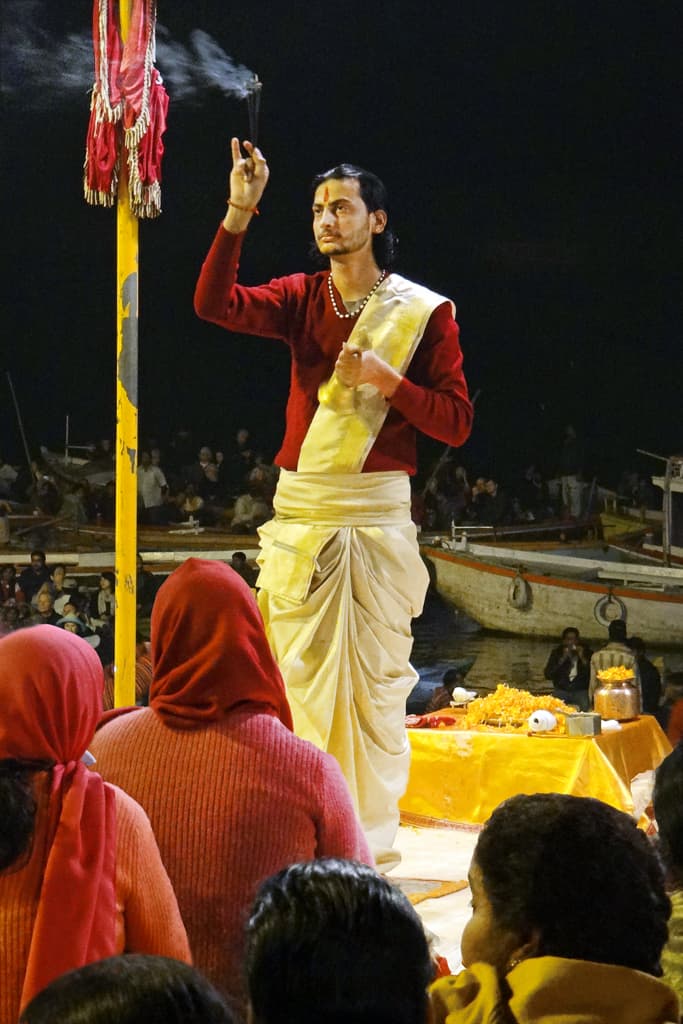 La cérémonie Ganga Ārtī (ici, l'un des sept brahmanes qui officient ensemble face au fleuve). Le Ganga Ārtī ou āratī (hindi : आरती) est un rituel hindou dans lequel la lumière de mèches imbibées de ghî ou de camphre est offerte à la déesse Gange. Le Ganga Ārtī est exécuté chaque soir face au fleuve. Les bénédictions de la divinité ainsi célébrée se répandent alors sur ses fidèles, qui accompagnent le rituel de chants ārtī.  

Varanasi, autrefois appelée Bénarès, est située au bord du Gange, à la confluence des fleuves Varunā et Assī. C'est l'une des plus importantes villes sacrées de l'hindouisme. Son nom traditionnel est Kâshî, la cité lumineuse de Shiva. Varanasi est également connue comme la Ville-lumière et la Ville-du-Savoir, consacrée à Shiva. Le Linga-d'Eau y est vénéré.  

La ville est célèbre pour ses ghâts, qui sont des berges recouvertes de marches en pierre permettant aux dévots hindous de descendre au fleuve pour y pratiquer des ablutions et des pūjās. Sur certains ghâts, les crémations sont rituellement effectuées.  

Articles de Wikipedia sur Varanasi et références :  
- fr.wikipedia.org/wiki/Varanasi  
- Ouvrage : Mythes et Dieux de l'Inde, Daniélou, Flammarion, 1992  
- Article de Wikipedia sur la cérémonie Ārtī : en.wikipedia.org/wiki/Ārtī  
- Voir les films sur Youtube : youtu.be/RYpzkvzPv88