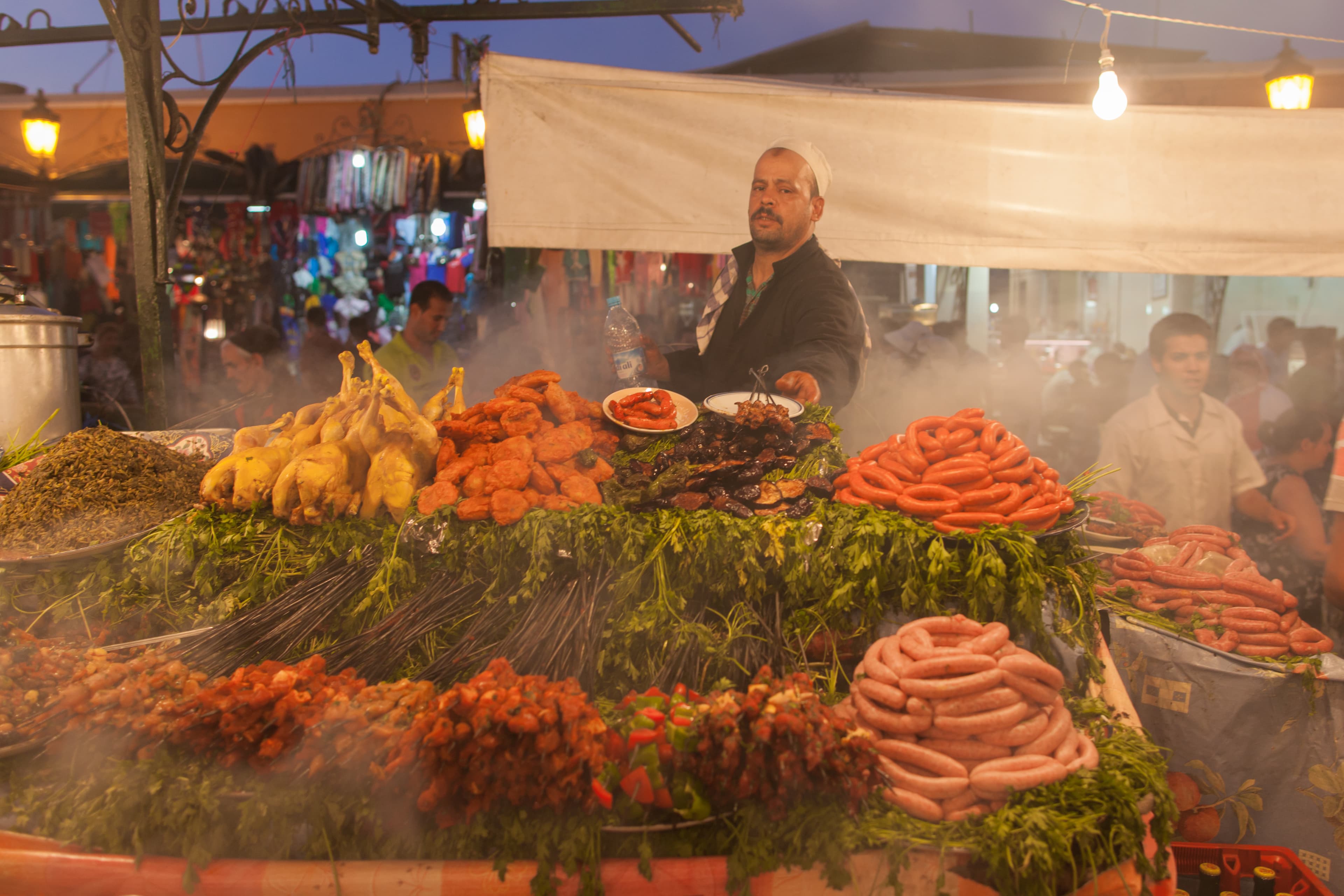 La place Jemaa el-Fna à Marrakech (Maroc). Coucher de soleil depuis la terrasse du "Café de France". Souk, vendeurs de jus d'orange pressé, de bijoux, charmeurs de serpents, artisanat marocain, souvenirs, tatouages au henné, restaurants de brochettes et merguez.