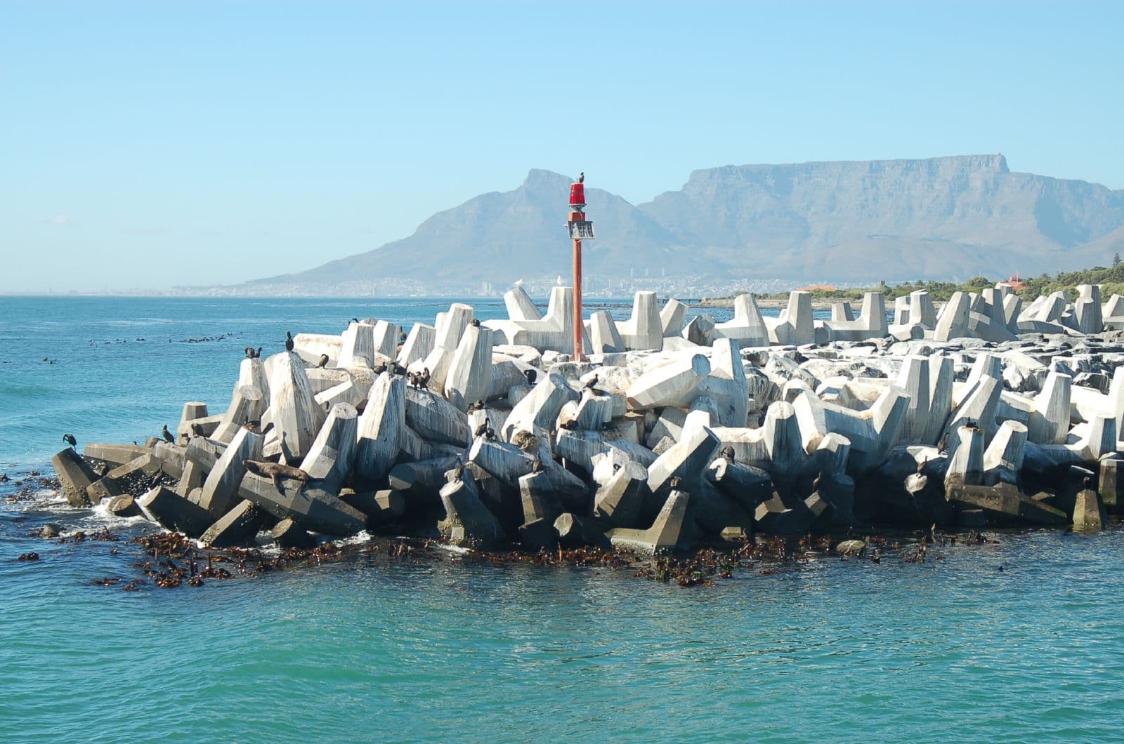 The breakwater of Robben Island prison is seen in the foreground, with Cape Town visible in the distance, behind this man-made barrier.