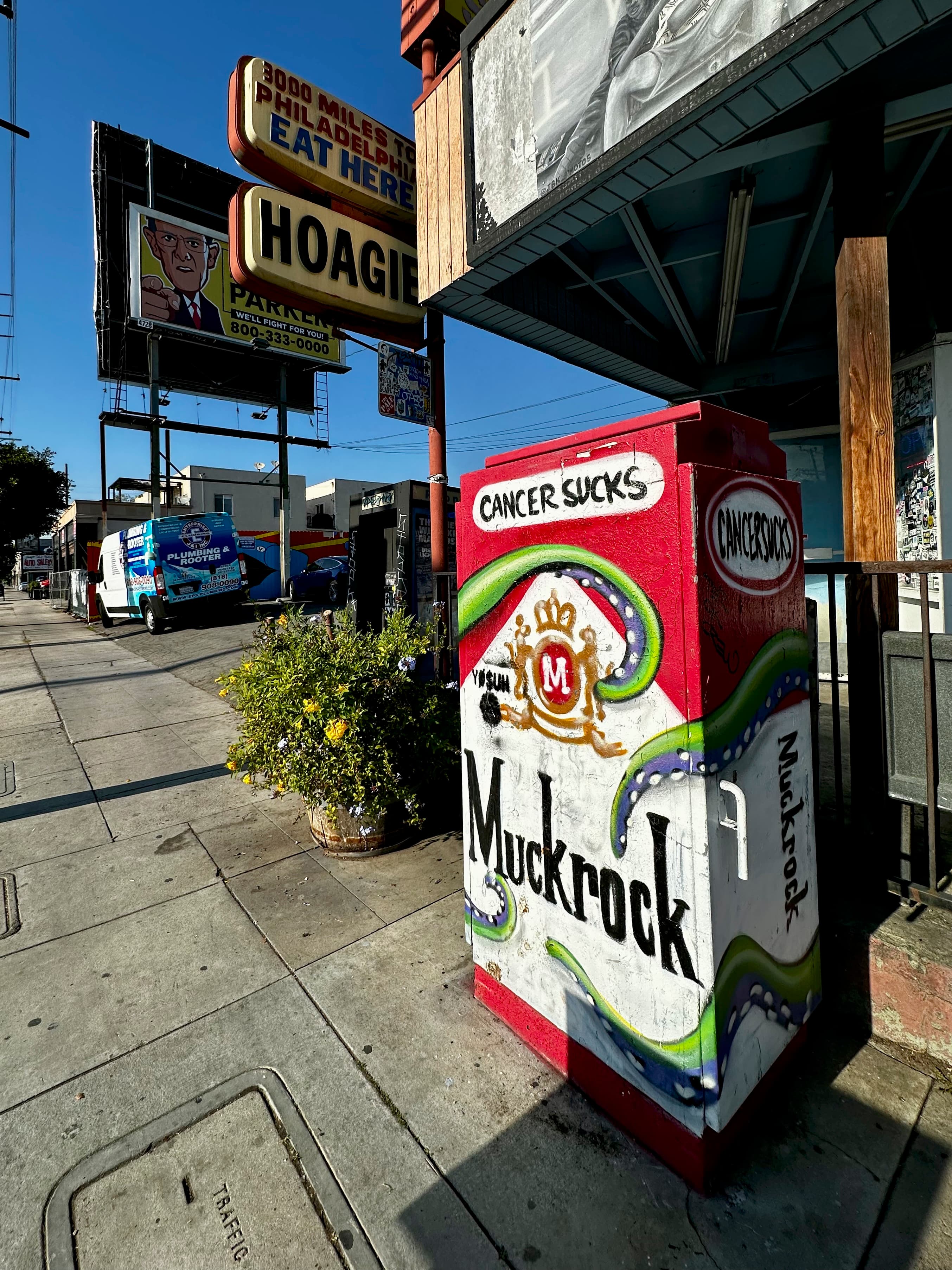 A utility box on Lincoln, in front of Great Western, is painted in an iconic red scheme featuring the words "Muckrock" below "Cancer Sucks."